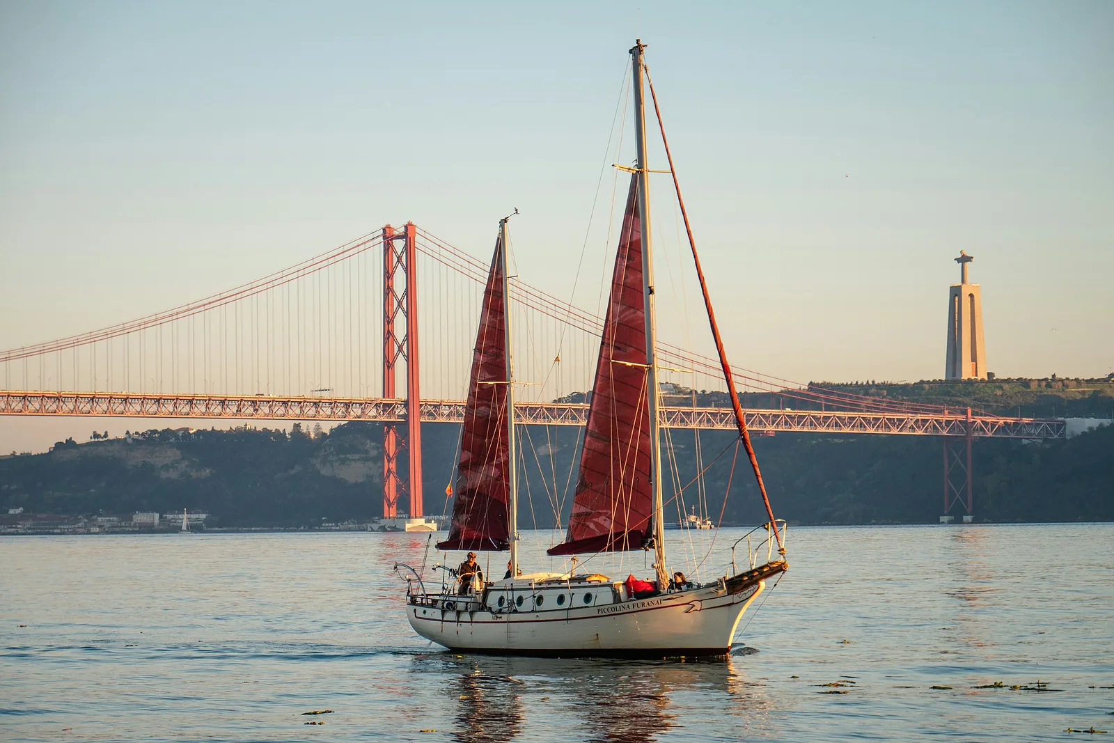 Un voilier aux voiles rouges sur le Tage, avec le pont du 25-Avril en arrière-plan